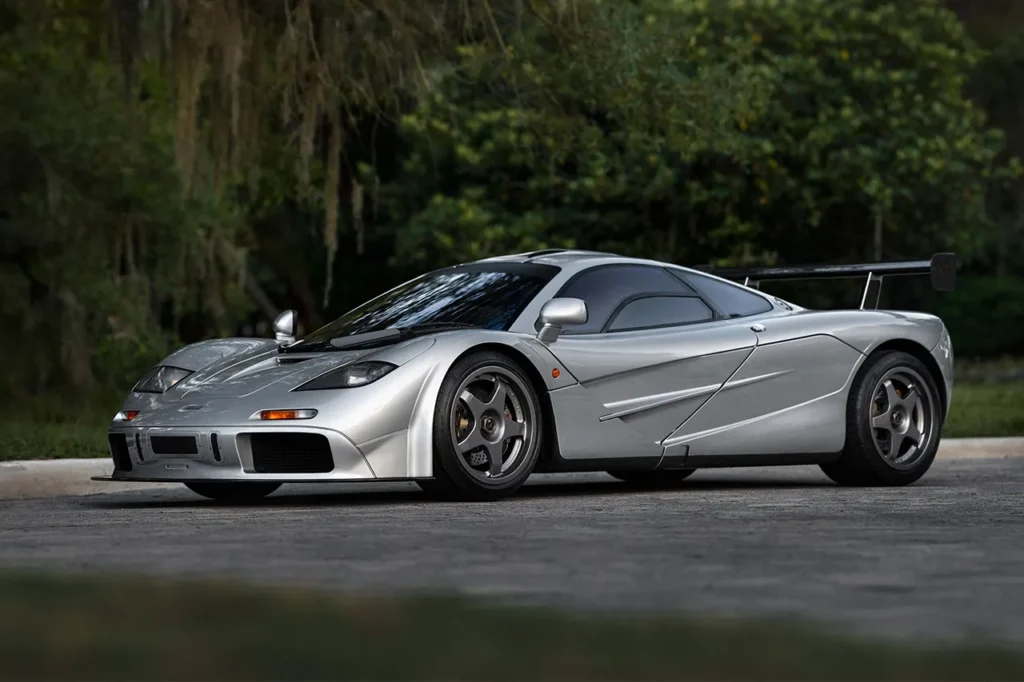 A silver McLaren F1 parked with a scenic green background, highlighting its timeless design and record-breaking performance